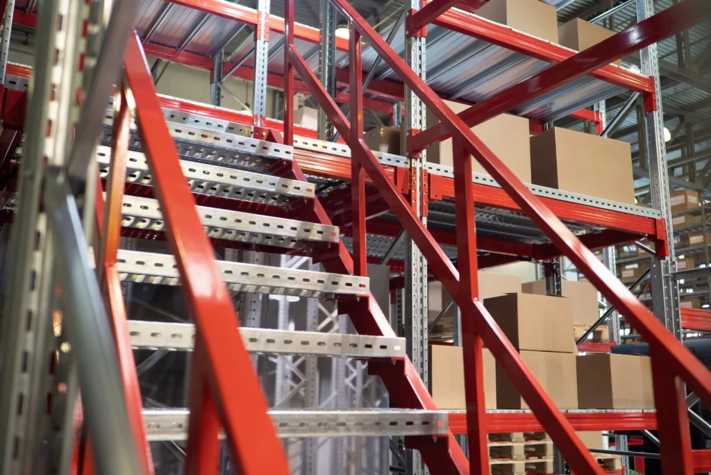 Escalier métallique rouge au milieu de rayonnages de stockage à plusieurs niveaux.