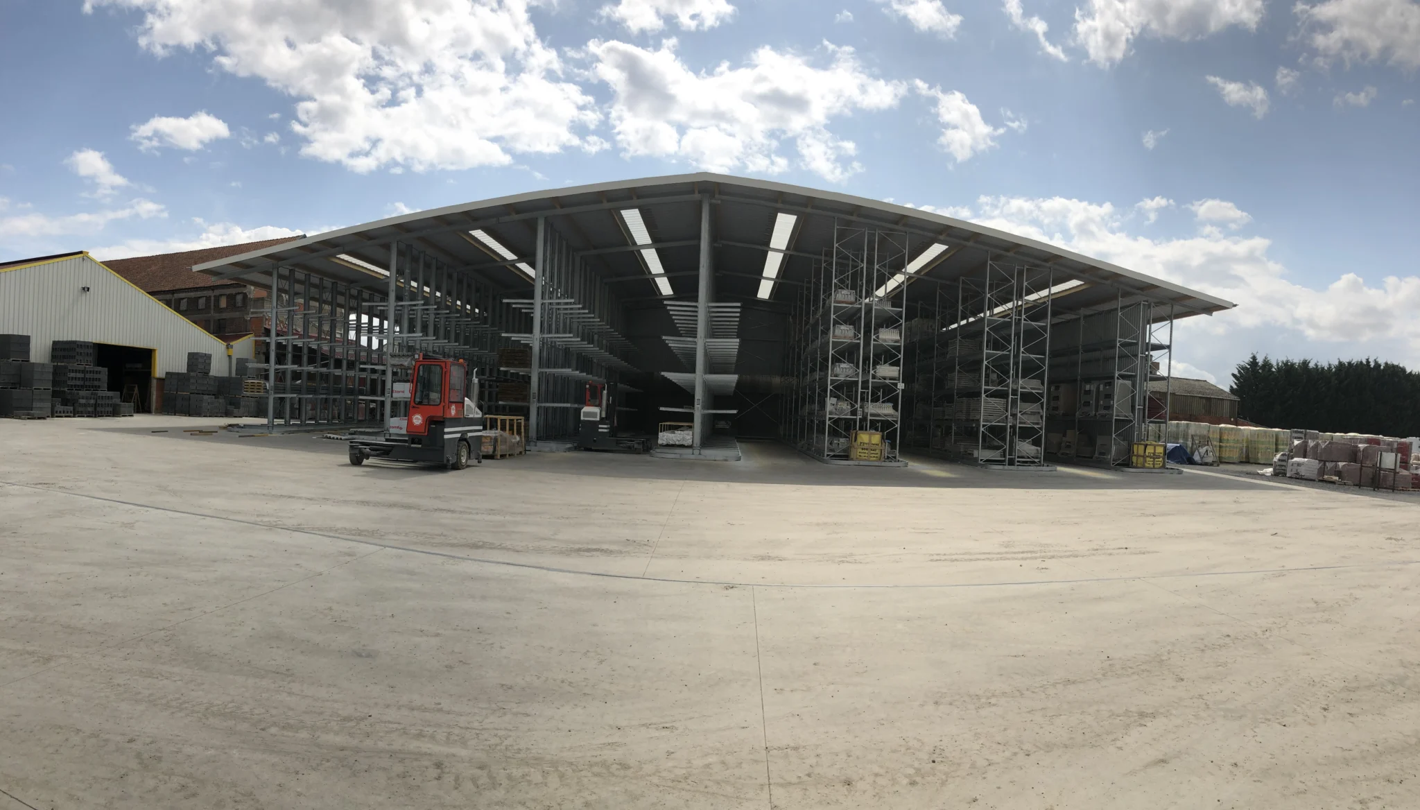 Hall de stockage avec cantilevers au centre, rayonnages à palettes à droite et chariot de manutention devant les allées.